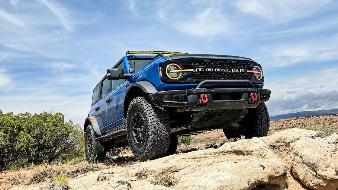 Hero shot of a Blue Ford Bronco with green trees behind it. 