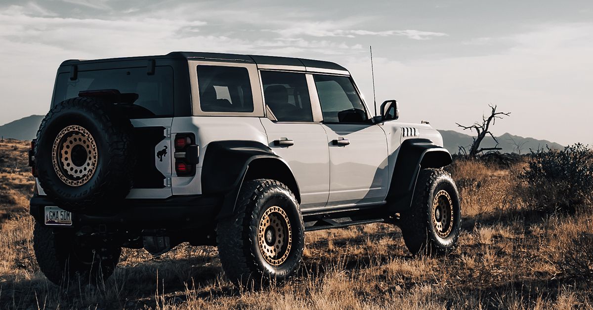 A white off-road SUV with a black soft top and large off-road tires parked in a dry grassy field with hills in the background.