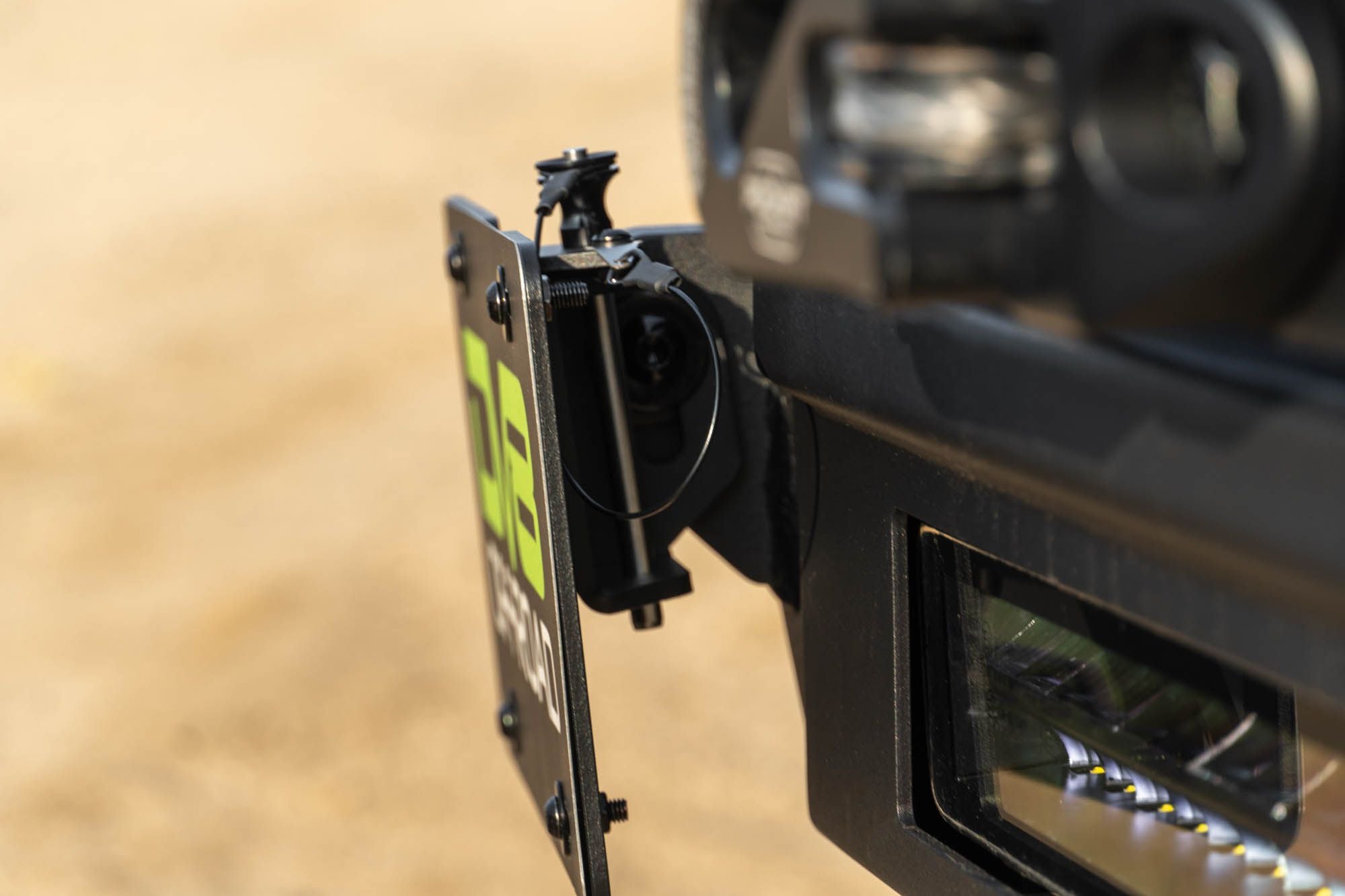 DV8 Offroad universal D-ring license plate mount installed on bumper close-up showing quick-release D-ring attachment