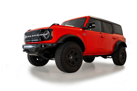 Addictive Desert Designs Stealth Fighter front bumper installed on orange 4-door Ford Bronco, distant front three-quarter view of full vehicle, product shot on white background