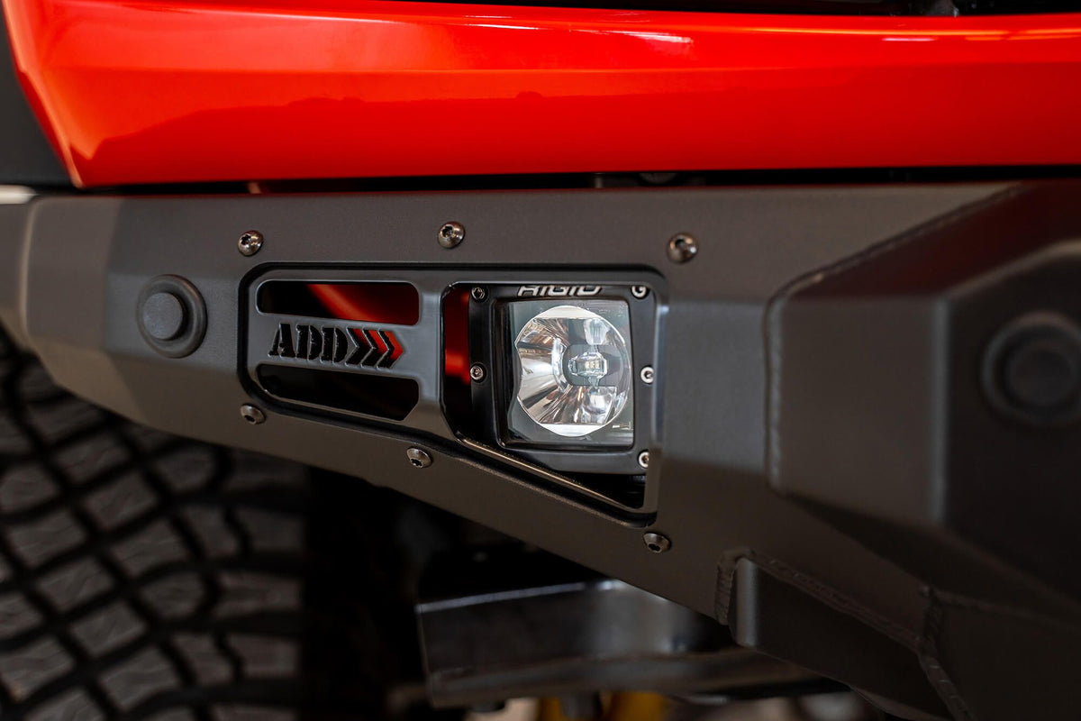 Addictive Desert Designs Stealth Fighter front bumper installed on Ford Bronco, close-up showing ADD logo and light pod on bumper corner