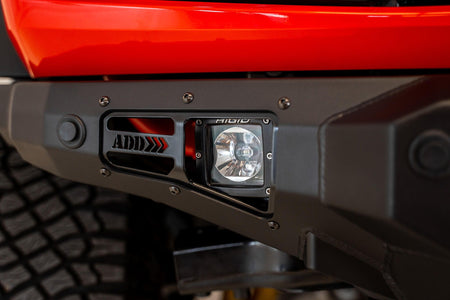 Addictive Desert Designs Stealth Fighter front bumper installed on Ford Bronco, close-up showing ADD logo and light pod on bumper corner