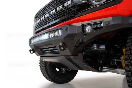 Addictive Desert Designs Stealth Fighter front bumper installed on orange Ford Bronco, close-up front three-quarter view product shot on white background