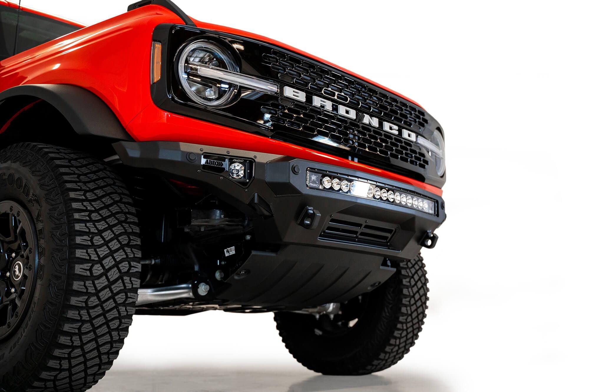 Addictive Desert Designs Stealth Fighter front bumper installed on orange Ford Bronco, front three-quarter close-up view, product shot on white background