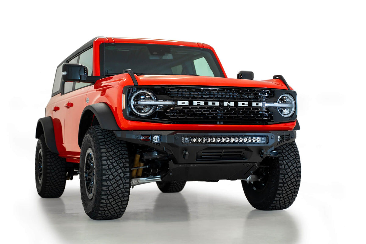 Addictive Desert Designs Stealth Fighter front bumper installed on orange Ford Bronco, front three-quarter view of full vehicle, product shot on white background