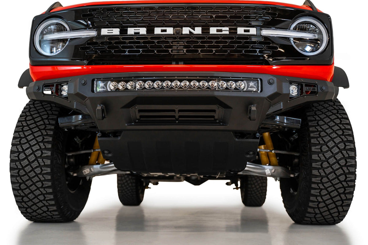 Addictive Desert Designs Stealth Fighter front bumper installed on orange Ford Bronco, straight-on close-up showing grille and light bar