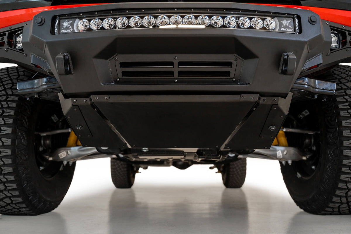 Addictive Desert Designs Stealth Fighter front bumper installed on Ford Bronco, underside close-up showing skid plate, product shot on white background