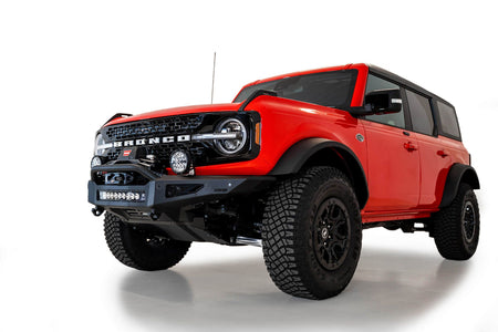 Addictive Desert Designs Rock Fighter winch front bumper installed on red 4-door Ford Bronco, front three-quarter view product shot on white background