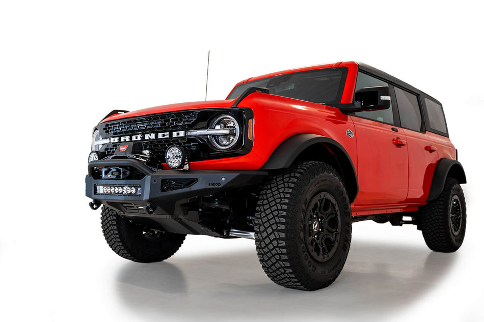 Addictive Desert Designs Rock Fighter winch front bumper installed on red 4-door Ford Bronco, front three-quarter view product shot on white background