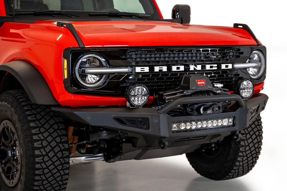 Addictive Desert Designs Rock Fighter winch front bumper installed on red Ford Bronco, close-up front three-quarter view showing winch and light bar
