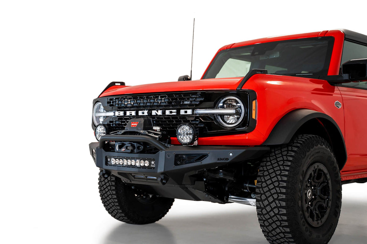Addictive Desert Designs Rock Fighter winch front bumper installed on red Ford Bronco, front three-quarter view product shot on white background