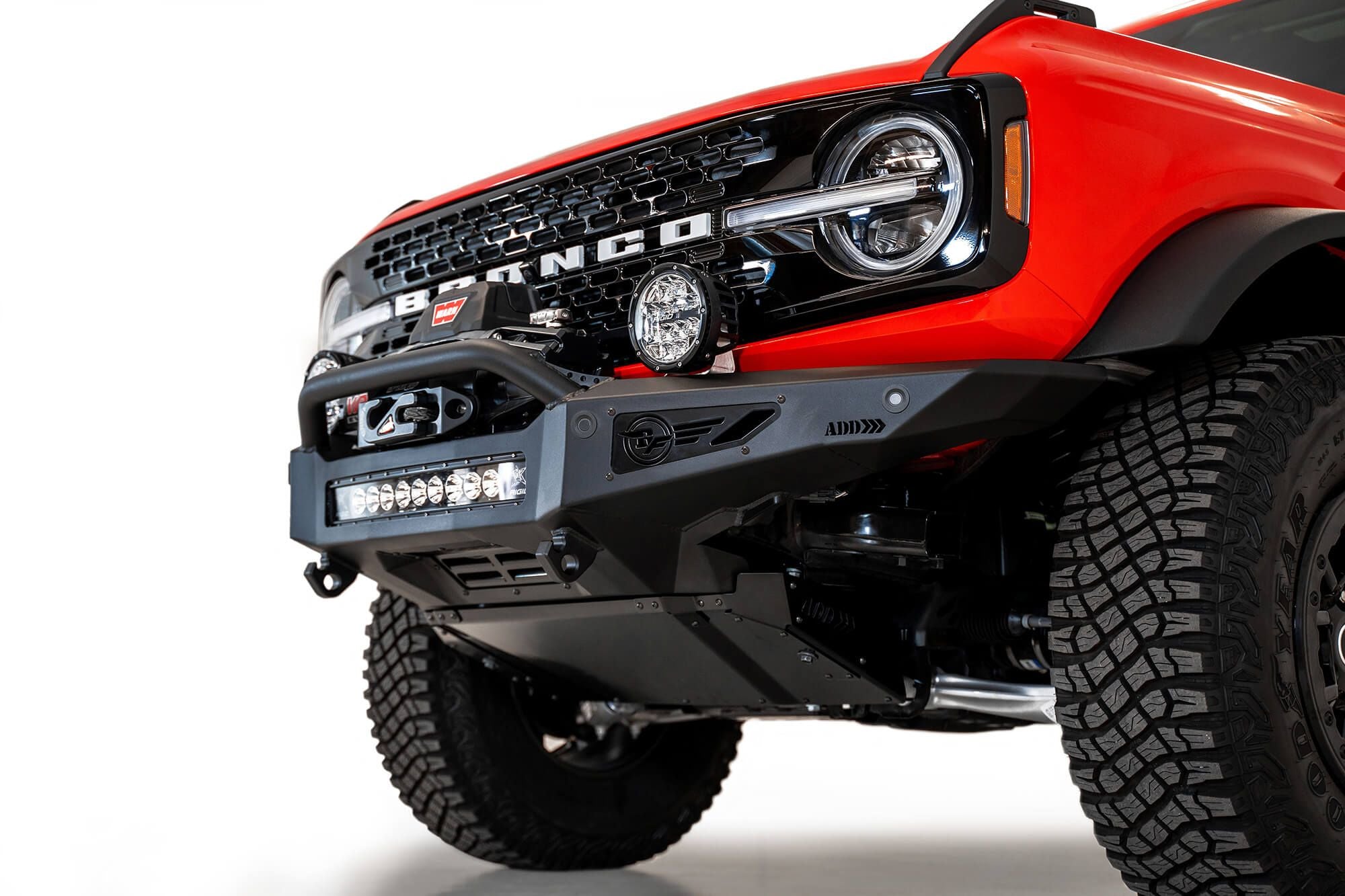 Addictive Desert Designs Rock Fighter winch front bumper installed on red Ford Bronco, low angle close-up showing winch and D-ring shackle mounts