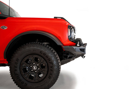 Addictive Desert Designs Rock Fighter winch front bumper installed on red Ford Bronco, side profile close-up showing fender and wheel