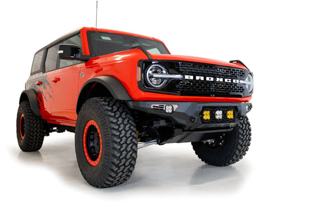 Addictive Desert Designs Bomber Baja front bumper installed on orange Ford Bronco, front three-quarter view showing full vehicle, product shot on white background