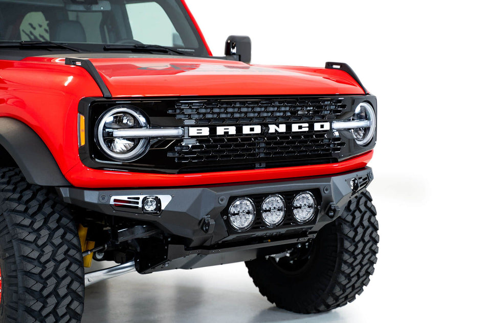 Addictive Desert Designs Bomber Rigid front bumper installed on red Ford Bronco, close-up front three-quarter view showing three-light pod cluster