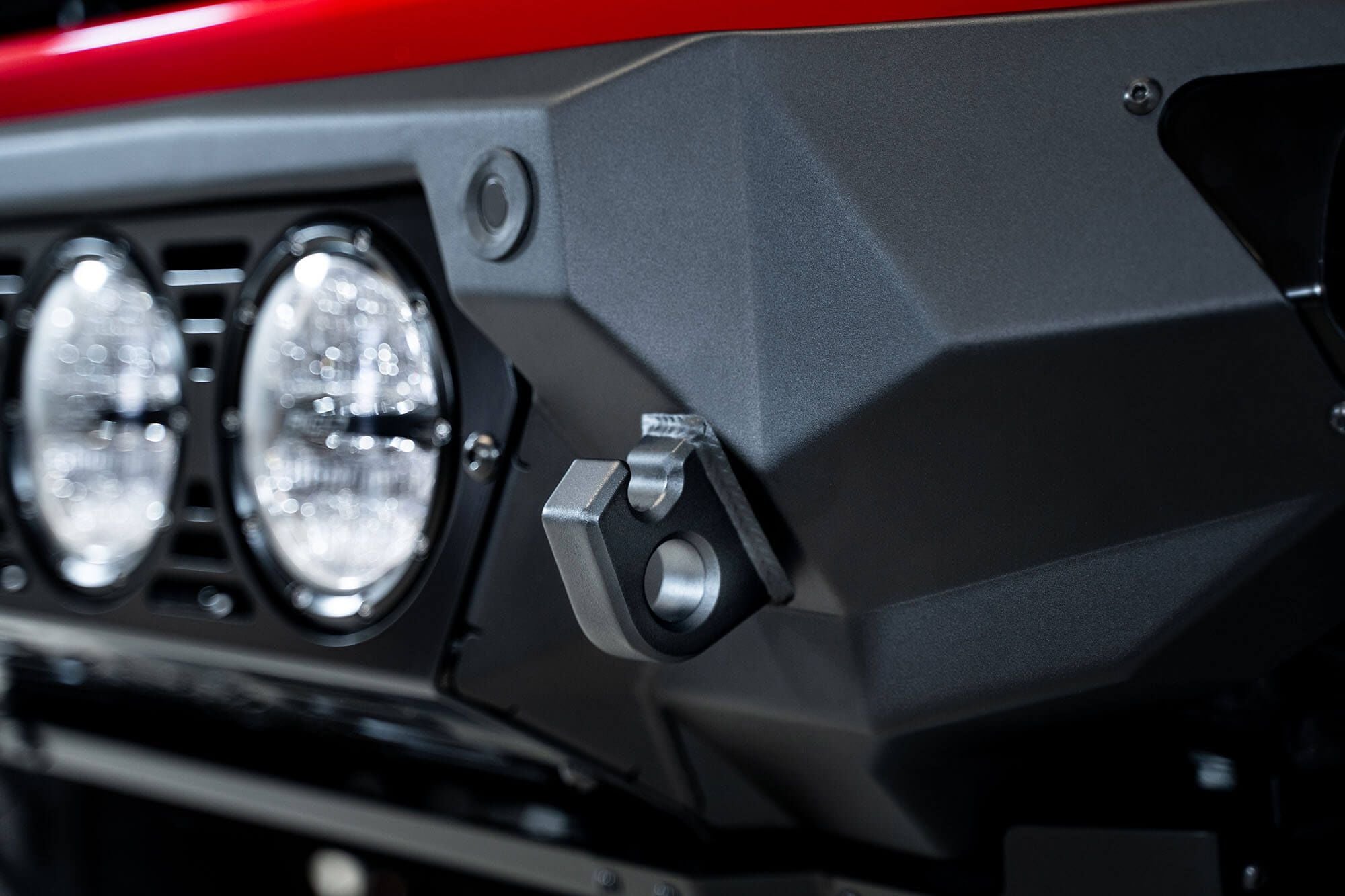 Addictive Desert Designs Bomber Rigid front bumper close-up showing round light pods on unpainted bumper section