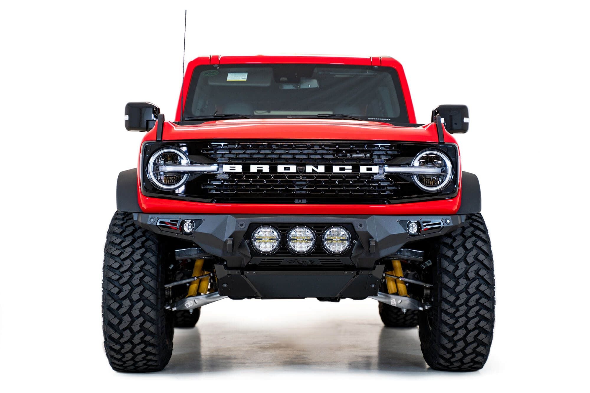 Addictive Desert Designs Bomber Rigid front bumper installed on red Ford Bronco, straight-on front view product shot on white background