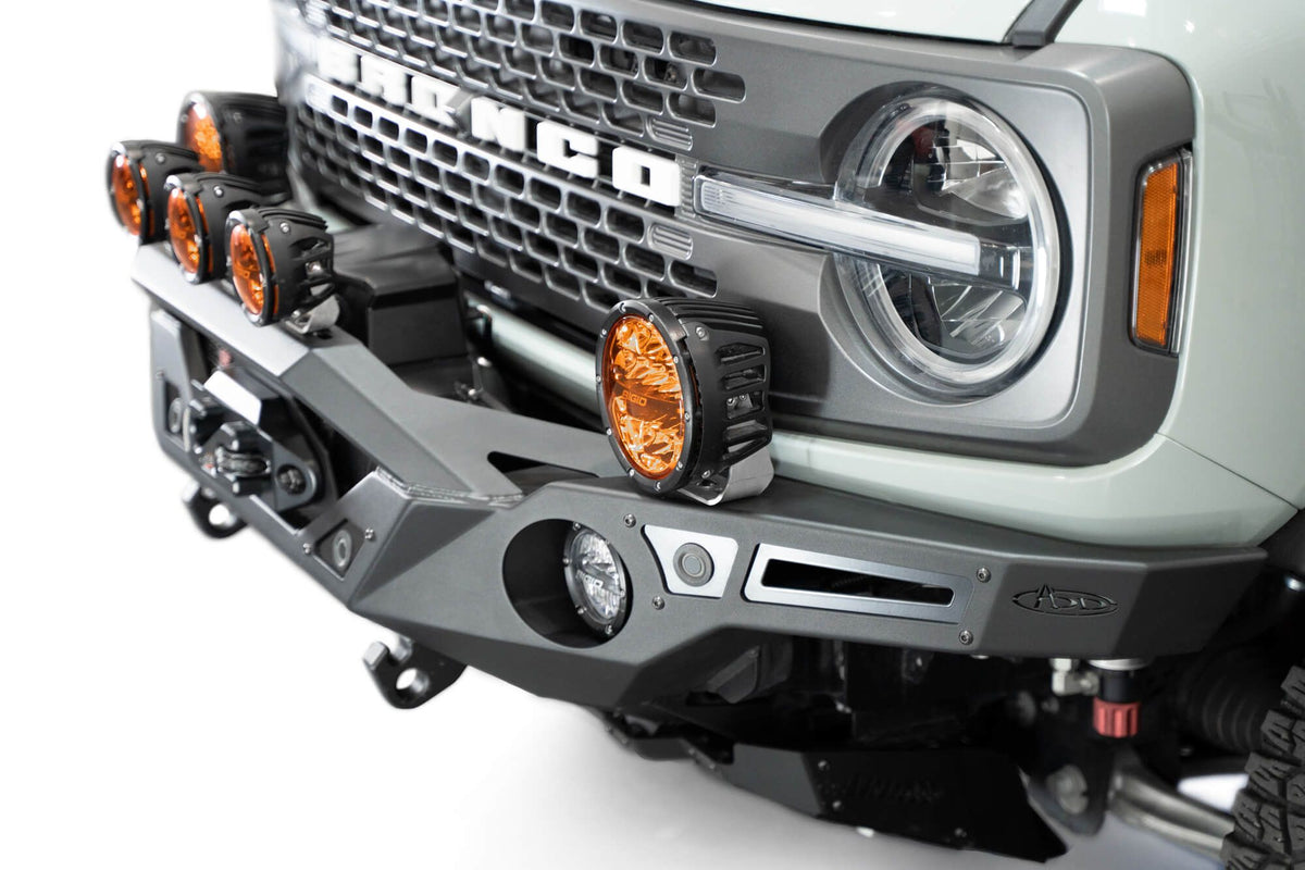 Addictive Desert Designs Krawler front bumper installed on gray Ford Bronco with amber marker lights, close-up showing bumper corner and headlight