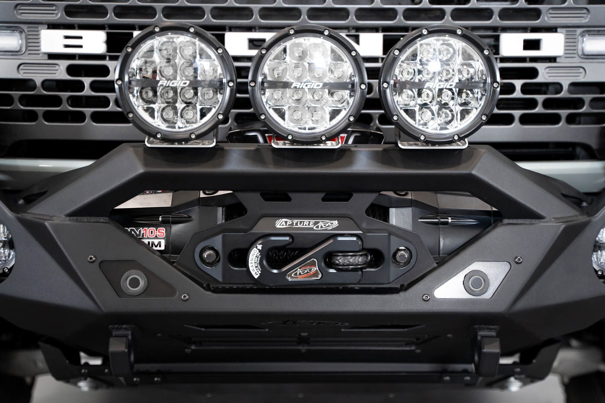 Addictive Desert Designs Krawler front bumper installed on gray Ford Bronco with amber marker lights, straight-on close-up showing full light row across bumper