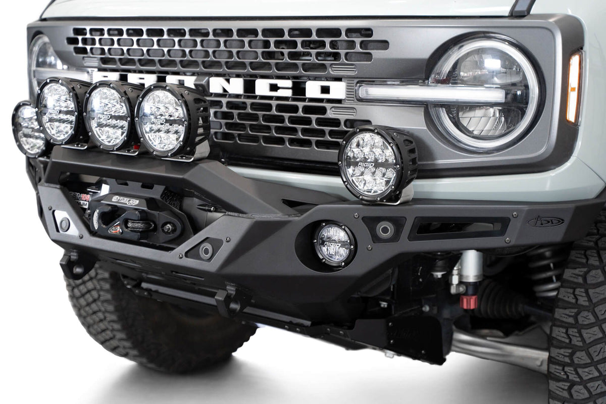 Addictive Desert Designs Krawler front bumper installed on gray Ford Bronco with amber marker lights, close-up showing grille and headlight