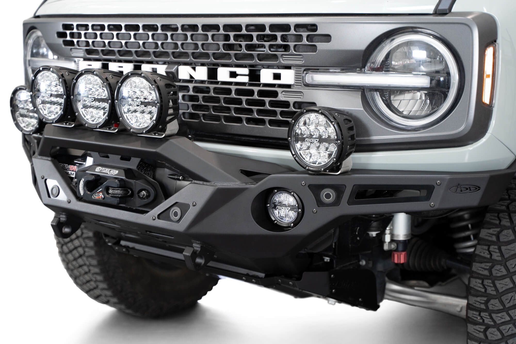 Addictive Desert Designs Krawler front bumper installed on gray Ford Bronco with amber marker lights, close-up showing grille and headlight