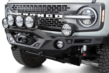 Addictive Desert Designs Krawler front bumper installed on gray Ford Bronco with amber marker lights, close-up showing grille and headlight