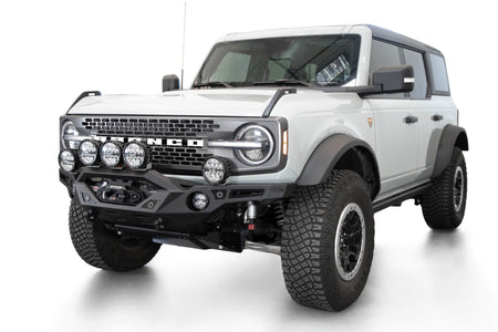 Addictive Desert Designs Krawler front bumper installed on white Ford Bronco with amber marker lights, front three-quarter view of full vehicle, product shot on white background