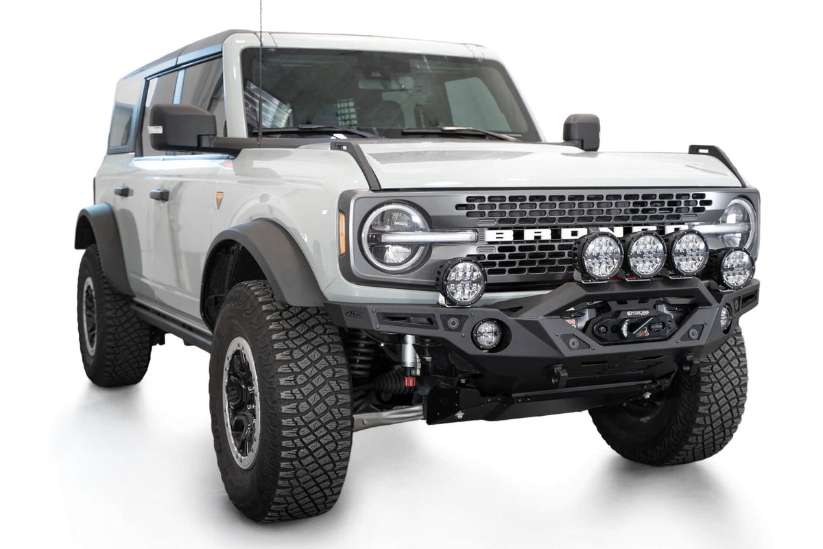 Addictive Desert Designs Krawler front bumper installed on gray Ford Bronco with amber marker lights, front three-quarter view of full vehicle, product shot on white background
