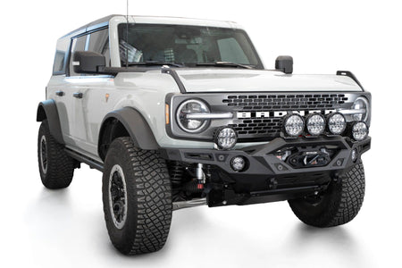 Addictive Desert Designs Krawler front bumper installed on gray Ford Bronco with amber marker lights, front three-quarter view of full vehicle, product shot on white background