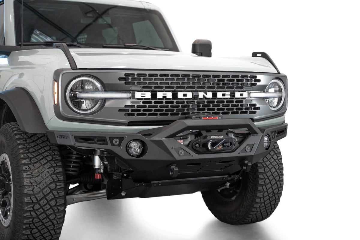 Addictive Desert Designs Krawler front bumper installed on gray Ford Bronco, close-up front three-quarter view showing integrated skid plate and light bar