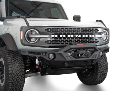 Addictive Desert Designs Krawler front bumper installed on gray Ford Bronco, close-up front three-quarter view showing integrated skid plate and light bar