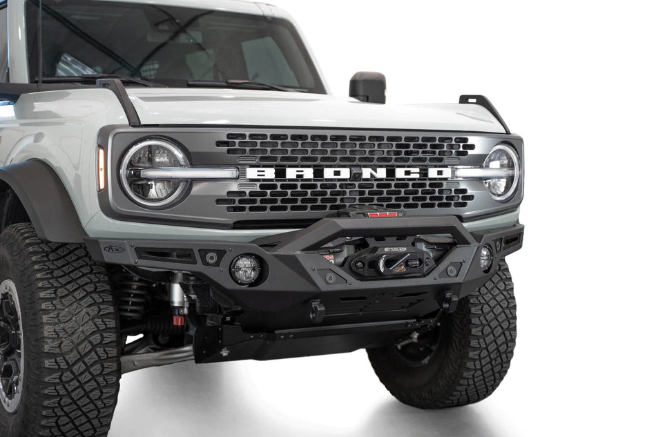Addictive Desert Designs Krawler front bumper installed on gray Ford Bronco, close-up front three-quarter view showing integrated skid plate and light bar