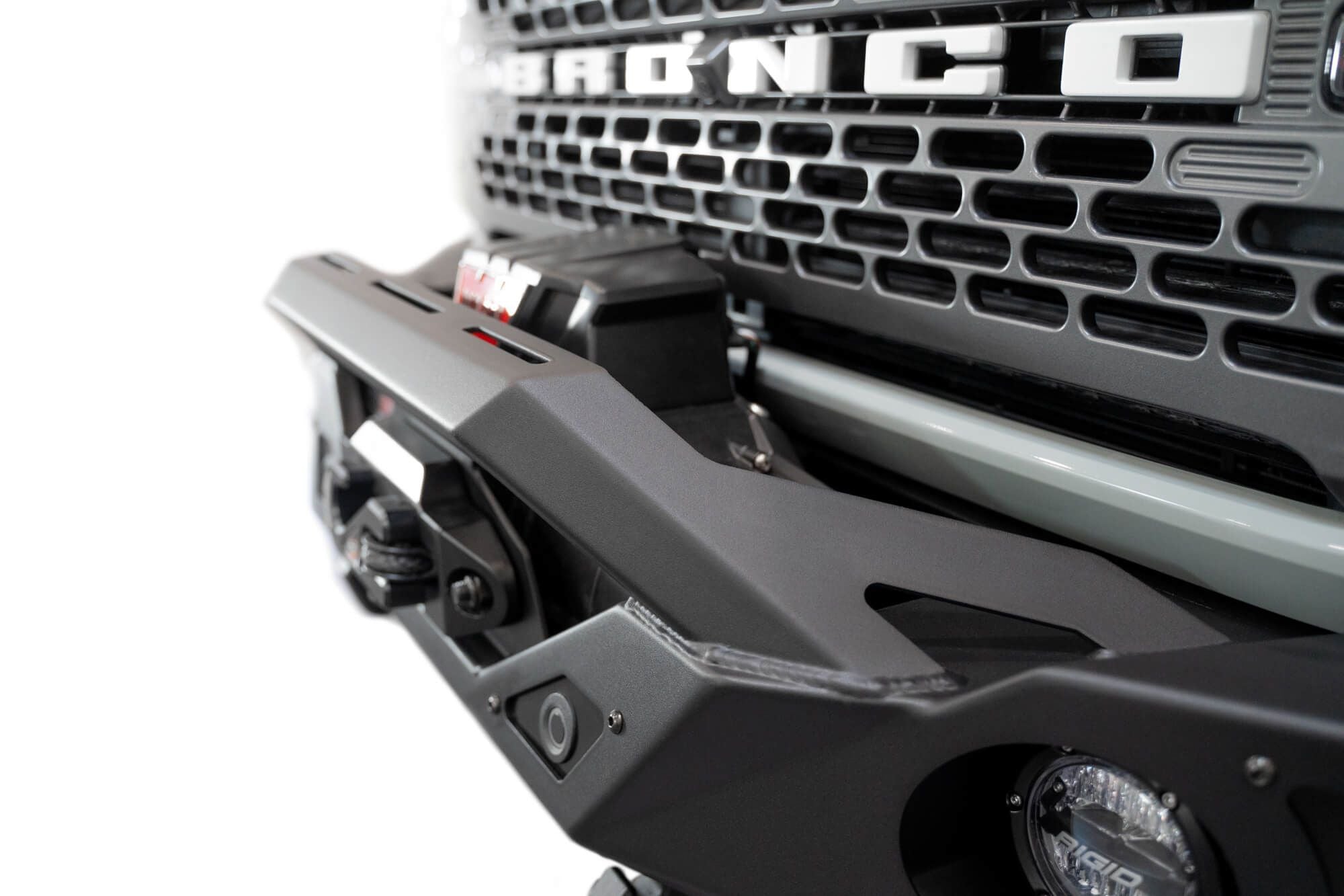 Addictive Desert Designs Krawler front bumper installed on gray Ford Bronco, close-up showing grille and bumper top edge