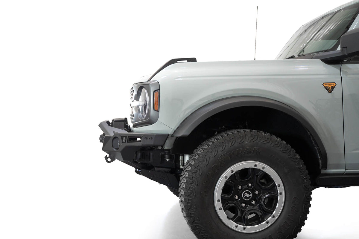 Addictive Desert Designs Krawler front bumper installed on gray Ford Bronco, close-up front three-quarter view showing grille and wheel
