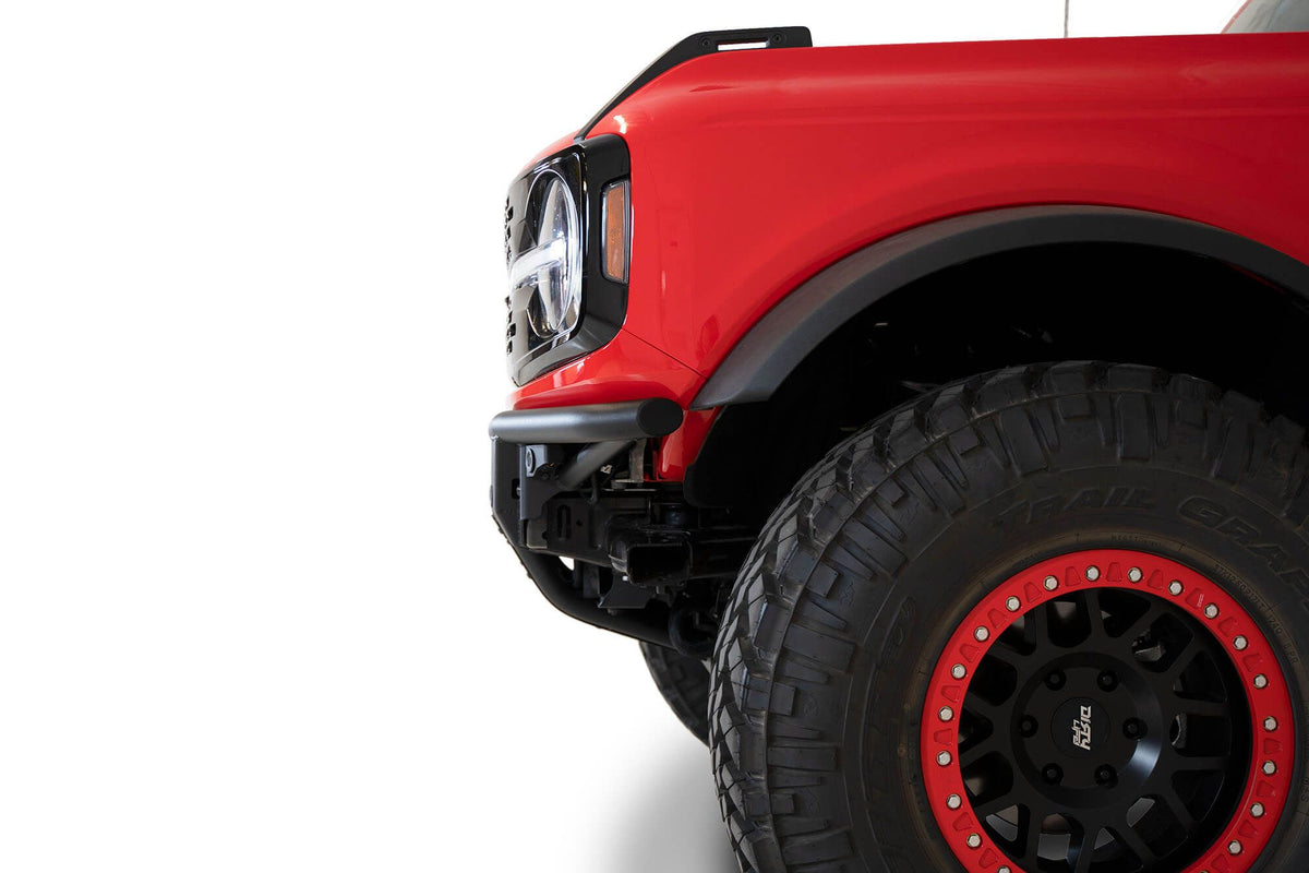 Addictive Desert Designs PRO Bolt-On front bumper installed on red Ford Bronco, close-up showing fender and red beadlock wheel