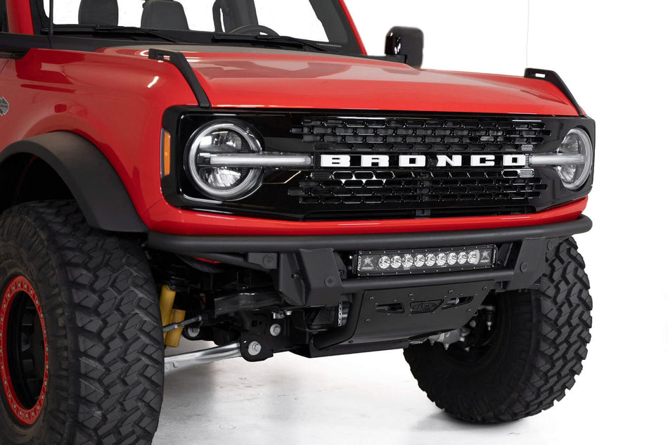 Addictive Desert Designs PRO Bolt-On front bumper installed on red Ford Bronco, close-up front three-quarter view showing light bar and shackle mounts