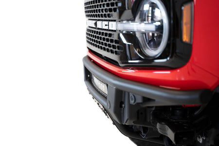 Addictive Desert Designs PRO Bolt-On front bumper installed on red Ford Bronco, close-up showing grille and headlight