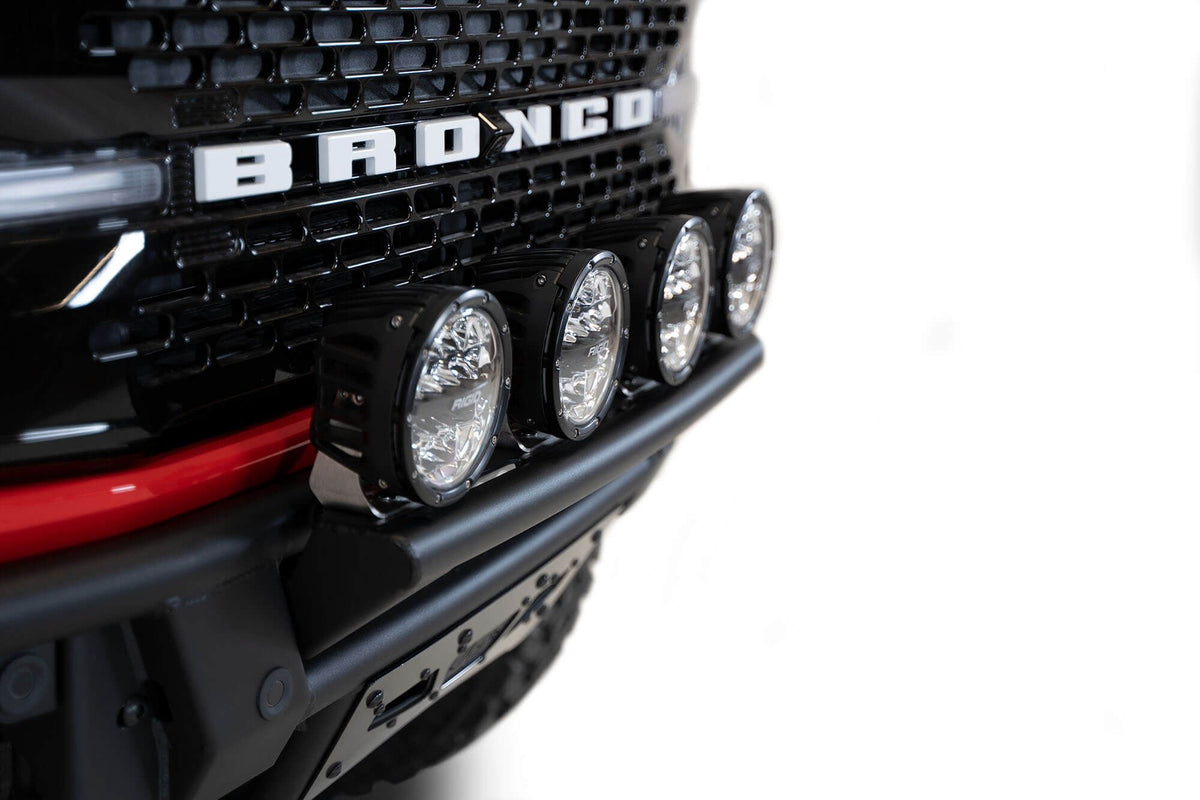 Addictive Desert Designs PRO Bolt-On front bumper installed on red Ford Bronco, straight-on close-up showing light bar and BRONCO grille badge