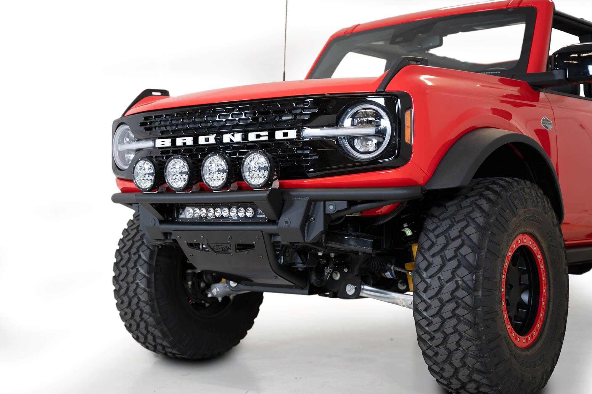 Addictive Desert Designs PRO Bolt-On front bumper installed on red Ford Bronco, front three-quarter close-up view product shot on white background