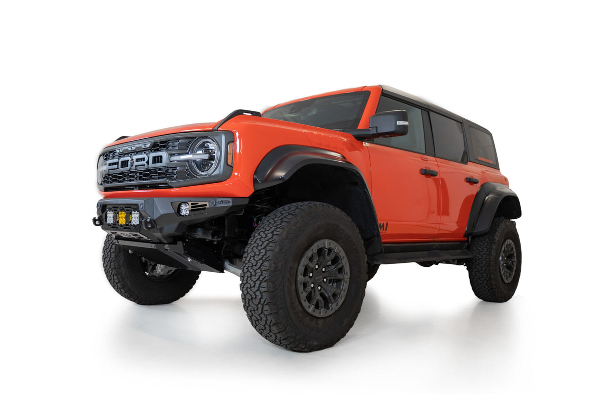 Addictive Desert Designs Bomber Baja front bumper installed on orange Ford Bronco Raptor, front three-quarter close-up showing grille and bumper