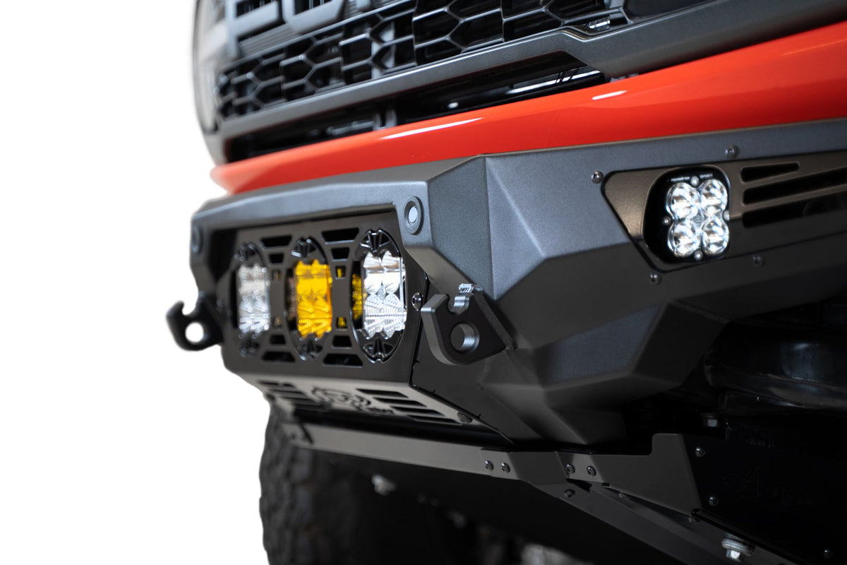 Addictive Desert Designs Bomber Baja front bumper installed on Ford Bronco Raptor, close-up showing amber and white light pod cluster