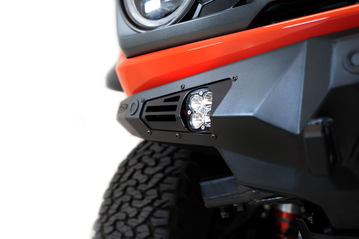 Addictive Desert Designs Bomber Baja front bumper installed on orange Ford Bronco Raptor, distant front three-quarter view of full vehicle on white background