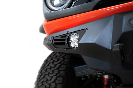 Addictive Desert Designs Bomber Baja front bumper installed on orange Ford Bronco Raptor, distant front three-quarter view of full vehicle on white background