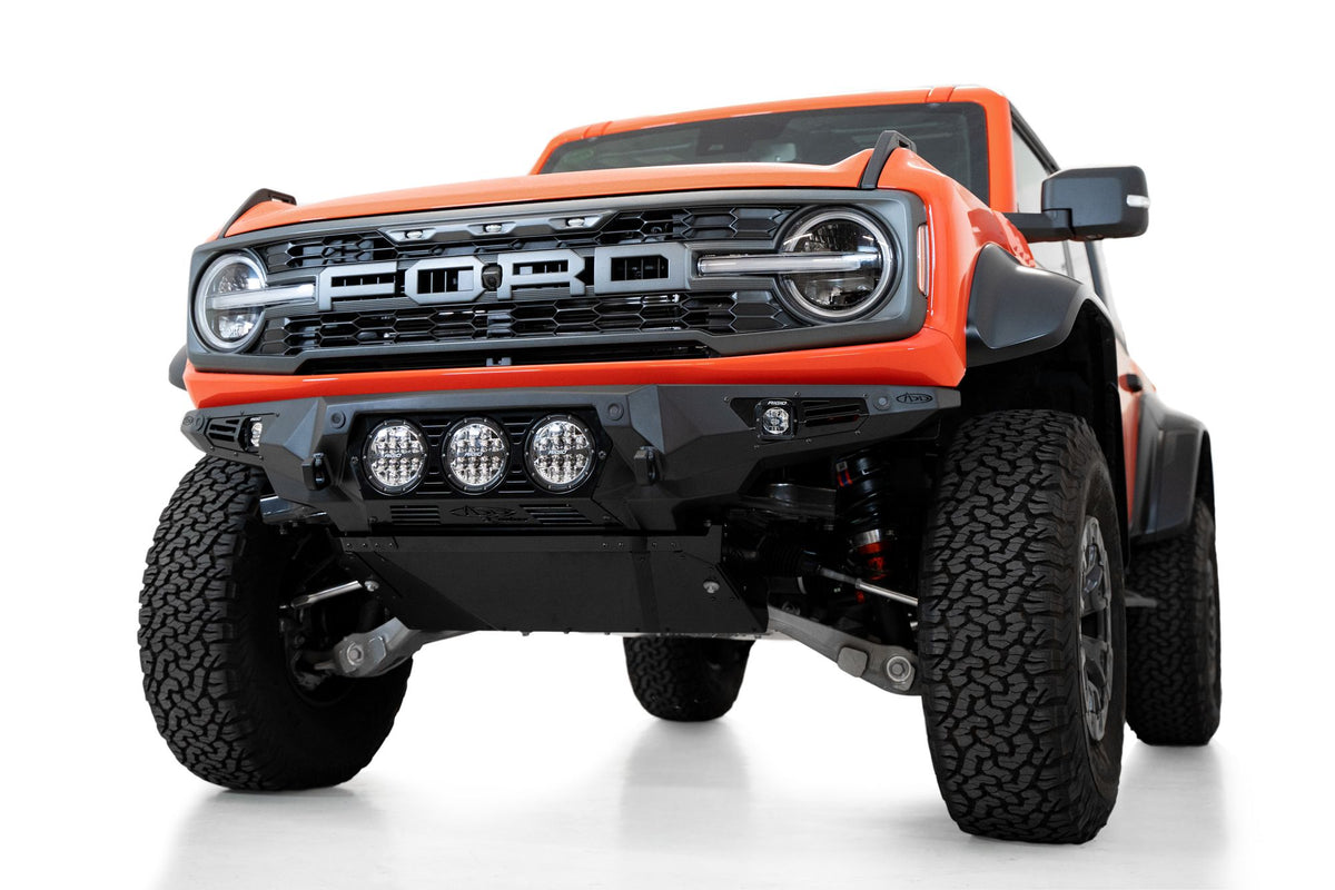 Addictive Desert Designs Bomber front bumper installed on orange Ford Bronco Raptor, alternate front three-quarter view product shot on white background