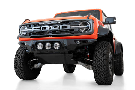 Addictive Desert Designs Bomber front bumper installed on orange Ford Bronco Raptor, alternate front three-quarter view product shot on white background