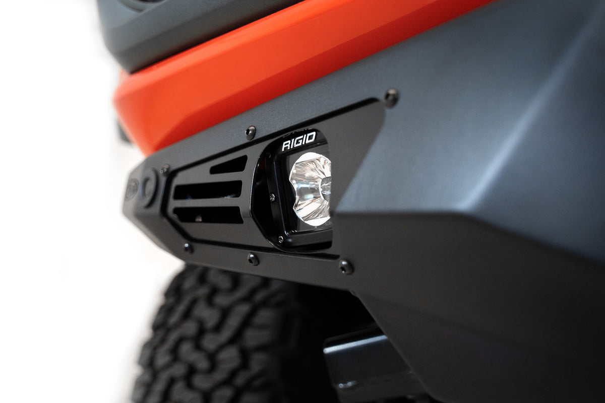 Addictive Desert Designs Bomber front bumper installed on Ford Bronco Raptor, close-up showing single integrated light pod on unpainted bumper section