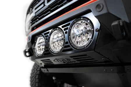 Addictive Desert Designs Bomber front bumper installed on Ford Bronco Raptor, straight-on close-up showing three-light pod cluster and grille