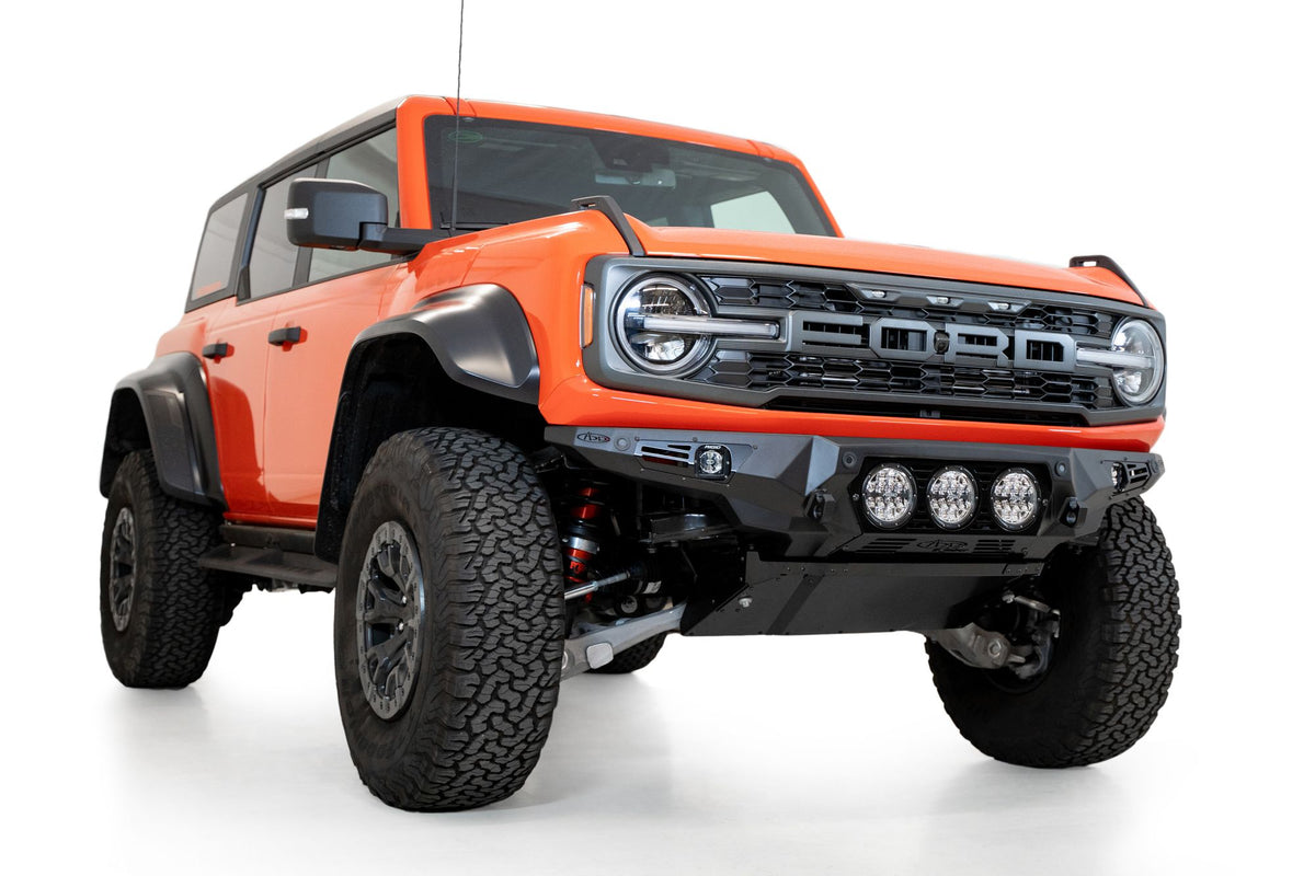 Addictive Desert Designs Bomber front bumper installed on orange Ford Bronco Raptor, front three-quarter view product shot on white background