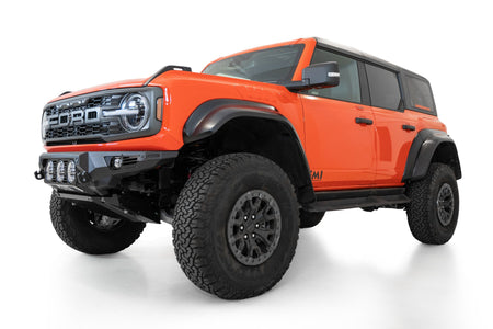 Addictive Desert Designs Bomber front bumper installed on orange Ford Bronco Raptor, rear three-quarter view of full vehicle product shot on white background