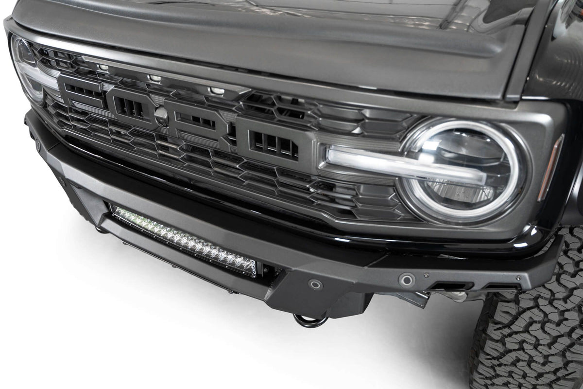 Addictive Desert Designs Phantom front bumper installed on black Ford Bronco Raptor, angled close-up showing bumper and light bar